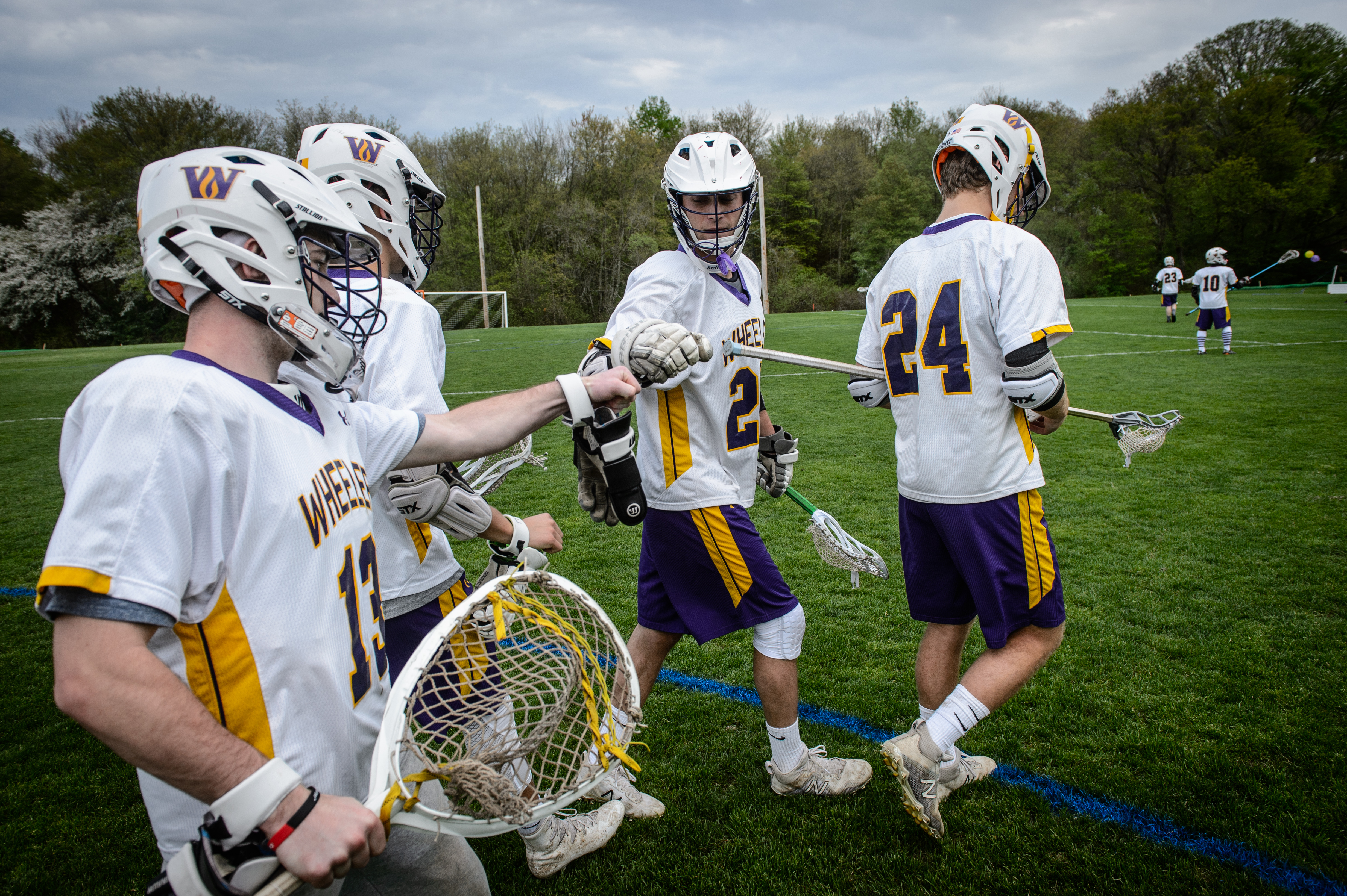 Boys lacrosse team members walk onto the field and fist bump each other.