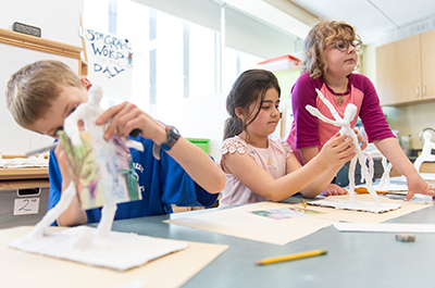 Three grade school children working at sculptures in an art studio.