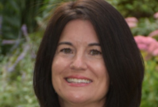 Closeup of the face of a white woman standing in front of flowers.