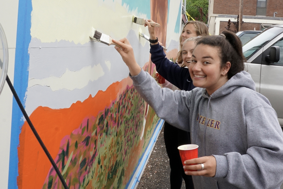Student artists smile as they work on an outdoor mural.