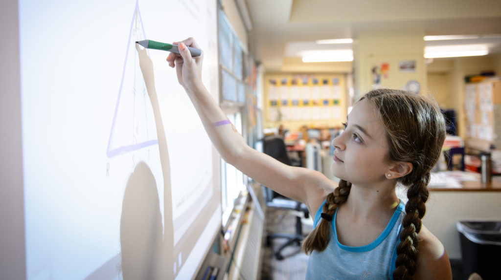 Girl elementary student at whiteboard drawing a triangle