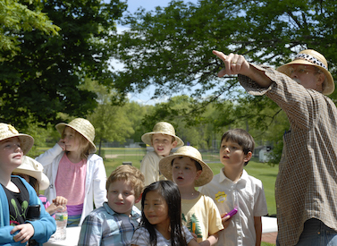 Aerie director Mark Harris wearing a pith helmet points into the distance while second graders, also wearing pith helmets, react on Safari Day.