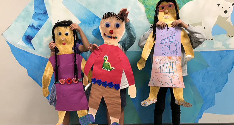 Three large paper dolls resembling the students who made them.