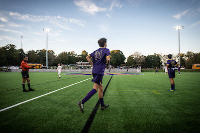 Player runs onto the turf field under the lights during a boys soccer game.
