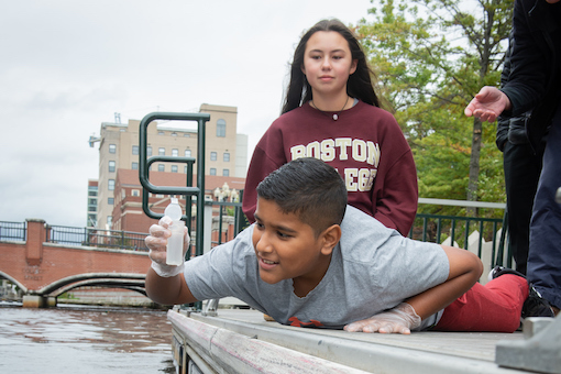 Boy examines a water sample from the river in downtown Providence while a classmate looks on.