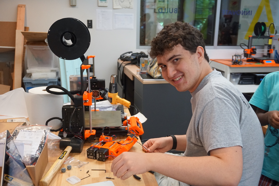 A high school boy smiles while working on a robotic device.