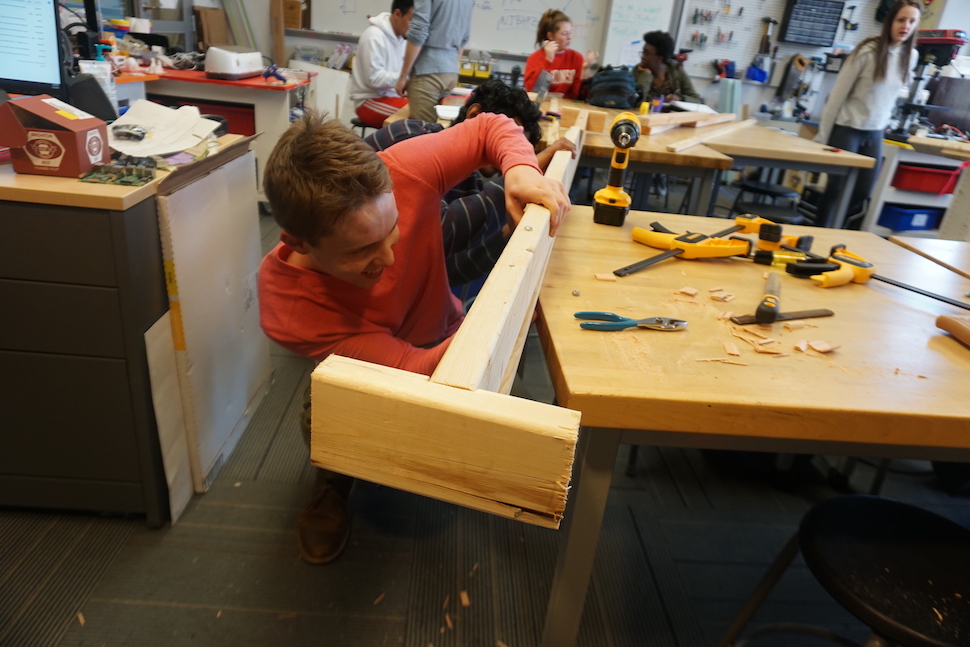 A student assembles pieces of lumber using hand tools in a maker's space.