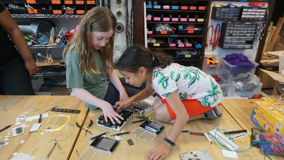 Two young girls work on the components to a robotic device.