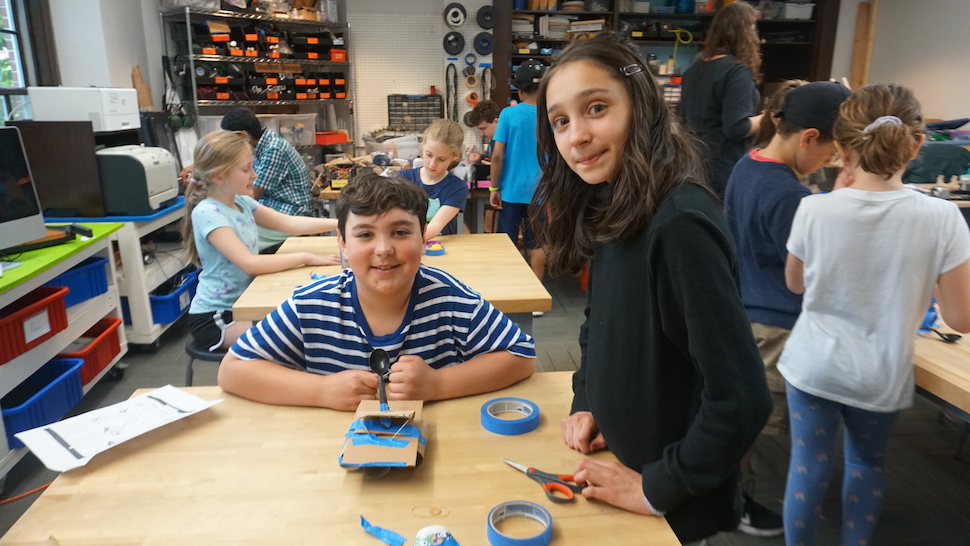 A group of young students work on engineering and machinery in a maker's space.