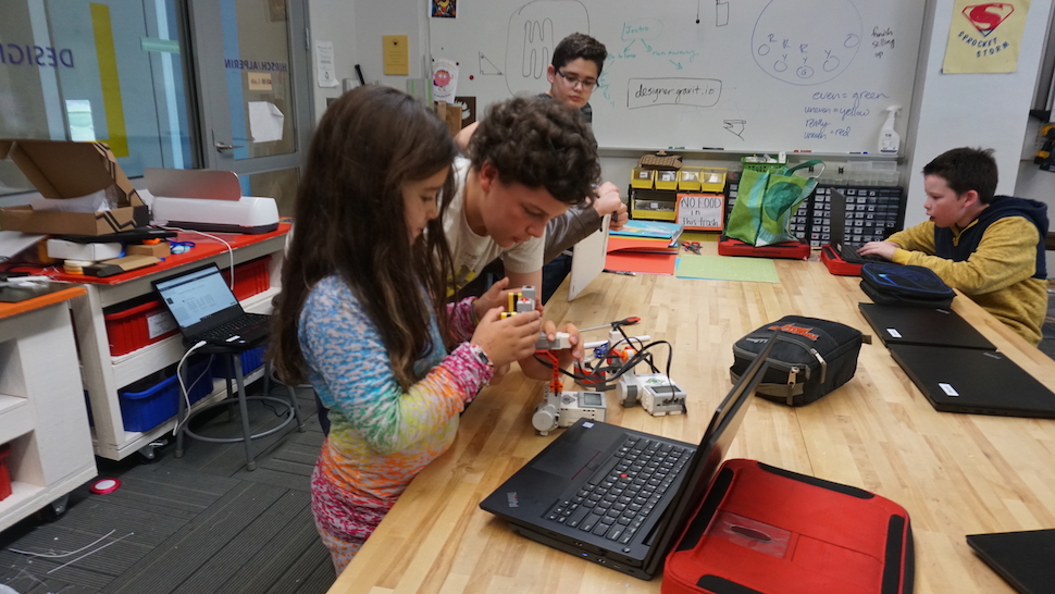 A young girl and an older boy work together on pieces of equipment in a maker's space.