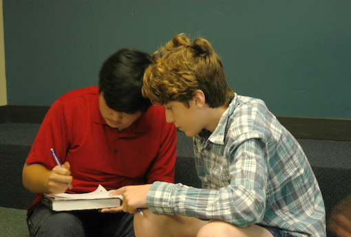 Two high school boys lean over a notepad as they collaborate on a project.