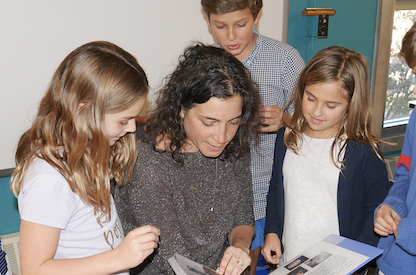 Head Allison Gaines Pell looks over a book with some elementary age students.