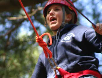 Young woman smiles delightedly while on a high ropes course in the woods.