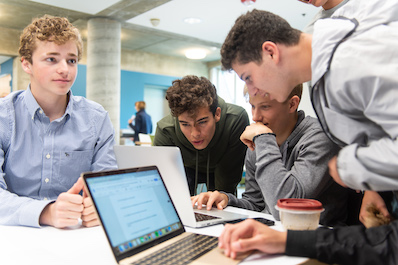 Group of high school boys gathering around laptops in the library