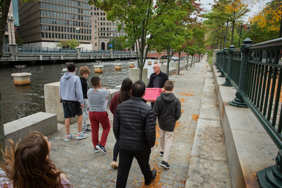 A group of students and teachers walk along the river's edge in downtown Providence.
