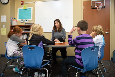 Teacher sits at a table with four students surrounding her.
