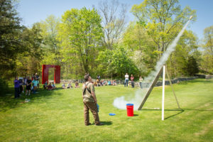 Teacher launches rocket outdoors as class looks on.