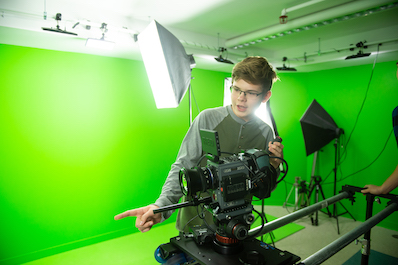 Boy works with camera in front of the Digital Production Studio green screen.