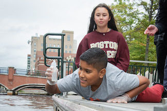 A boy pulls a water sample from a river in Providence while another student and teacher look on as part of the Cityside Program.