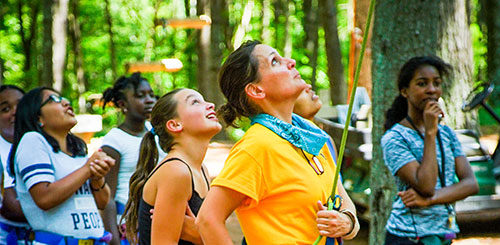 A ropes course coach looks up in the air with a group of students while holding a rope.