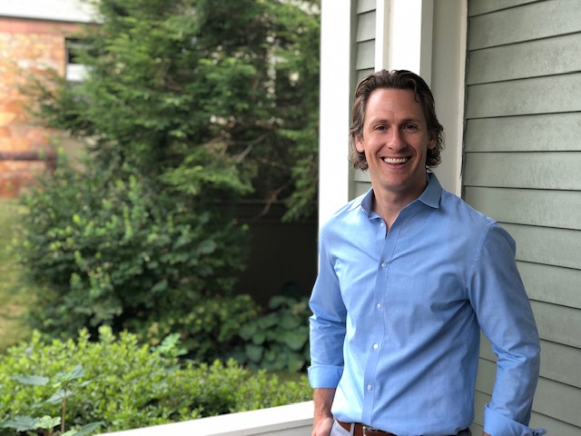 Enrollment staffer stands on porch of school building smiling