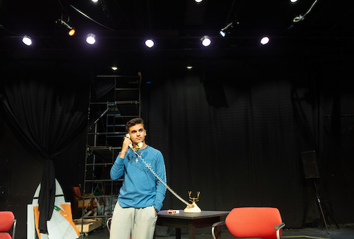 A student actor talks on an old landline phone on the set of a play.