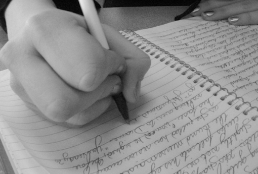 student's hand writing into a notebook.