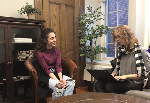 Student interviewed by reporter with laptop in campus office.