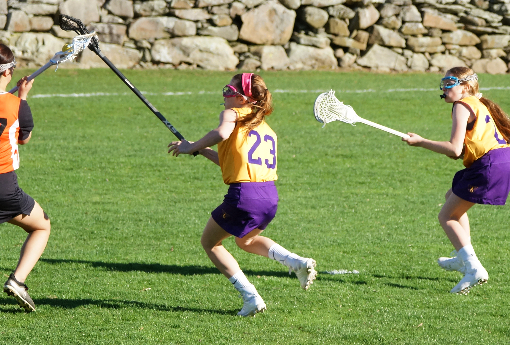 Two girls lacrosse players move down a field.