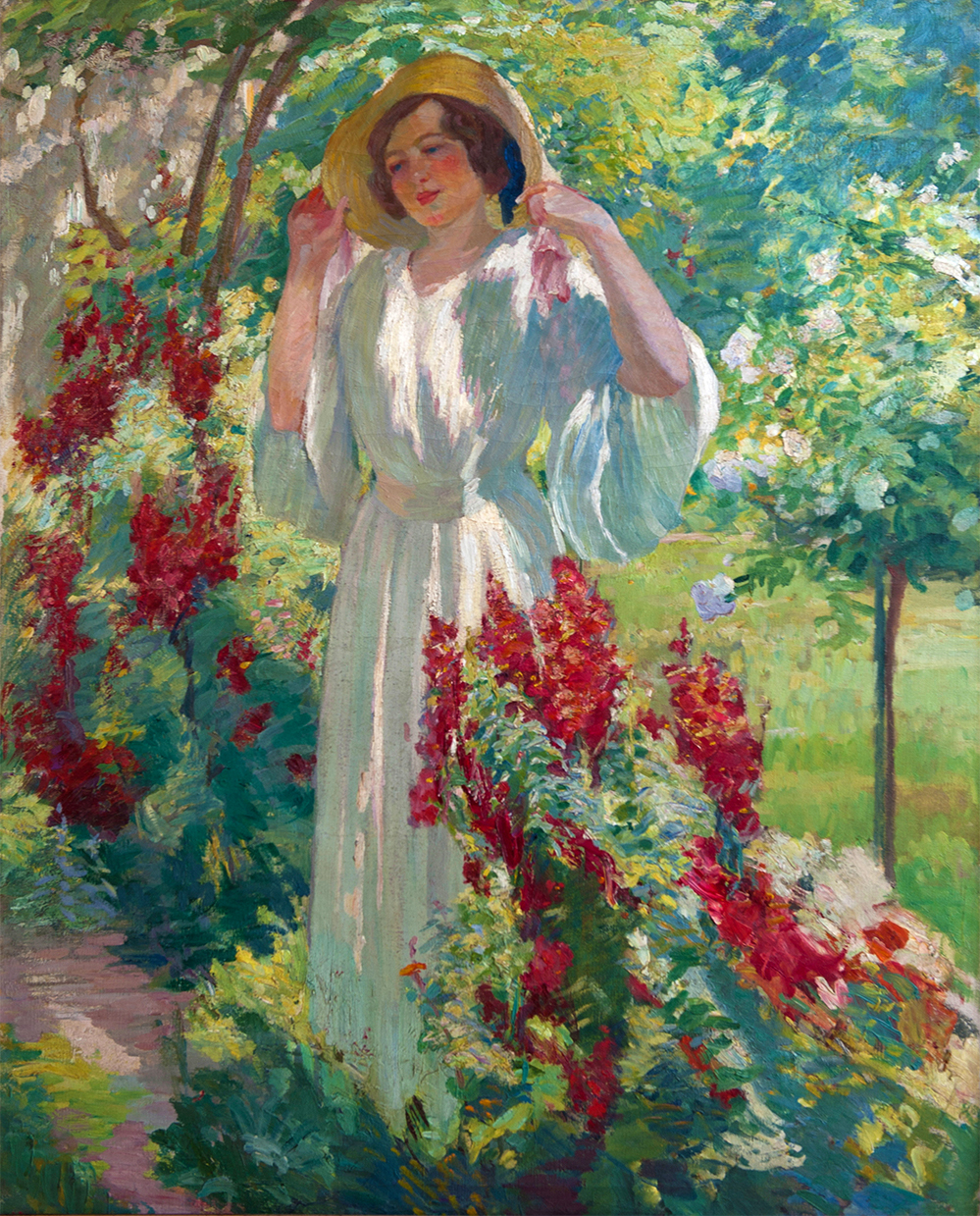 Portrait of a woman standing in a straw hat in a lush garden.