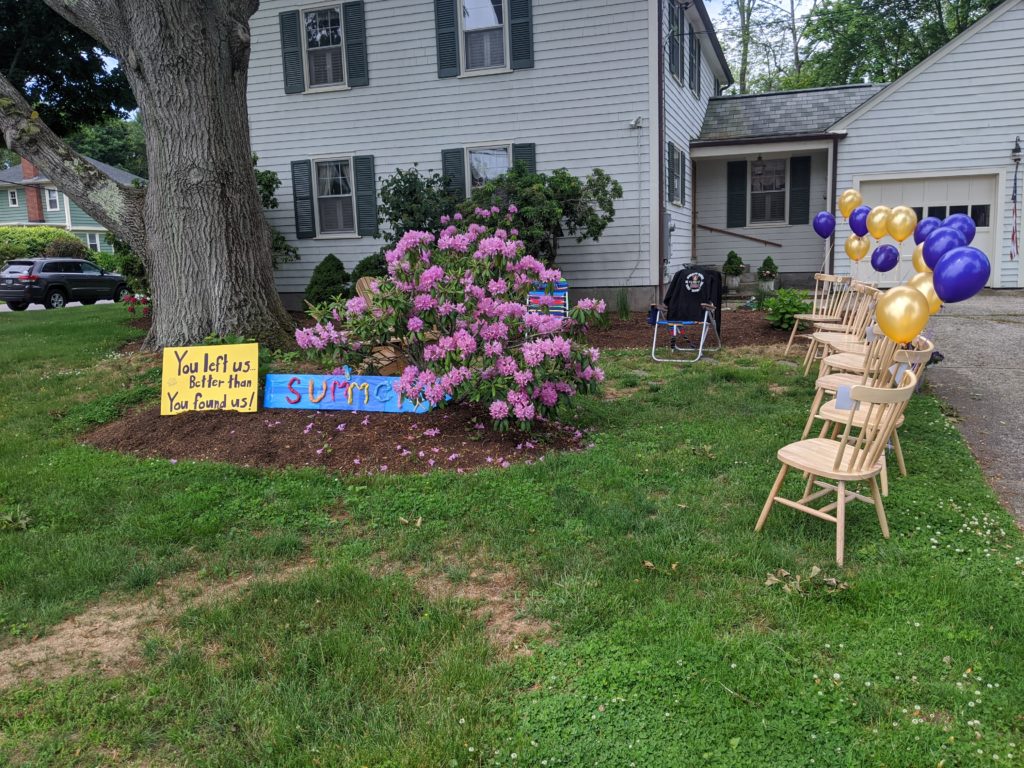 Chairs with purple and gold balloons and signs in a front yard congratulating Hamilton 8th graders on their graduation.