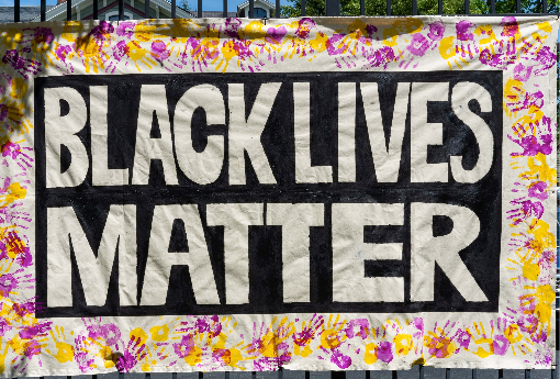 A banner stating Black lives matter hangs on the campus with purple and gold school color handprints surrounding it.