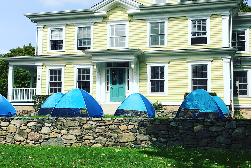 A row of small blue tents used for naptime set up in front of the yellow Columbine Hill House at the Wheeler Farm.