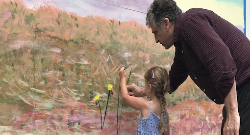 Teacher directs early childhood student as she paints flowers on a mural.