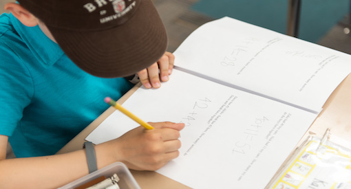 Young girl in Brown University ball cap, head bent over math workbook.