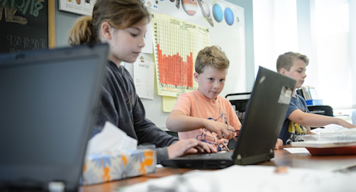 Girl and two boys sit at laptop computers entering data in a science classroom.