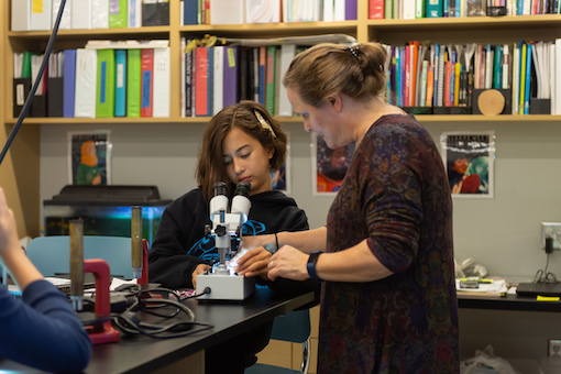 Female teacher helps middle school girl with special microscope in science lab.