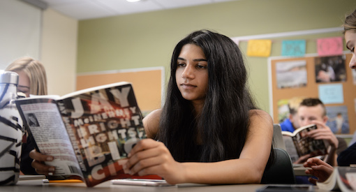 Dark-haired girl reads a book while in an English class with other reading students.