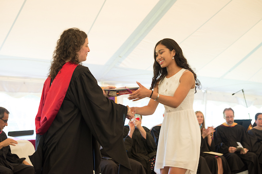 Female student smiles as she crosses graduation stage to accept her diploma from the Head of School.