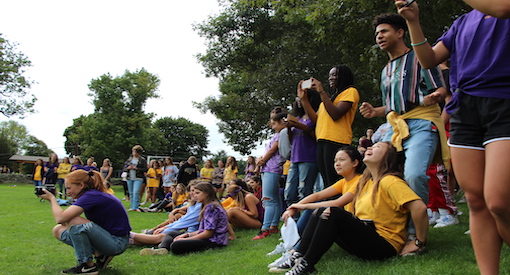 Group of high school students wearing purple and gold tee shirts sitting and standing on the sidelines at the Wheeler Farm.