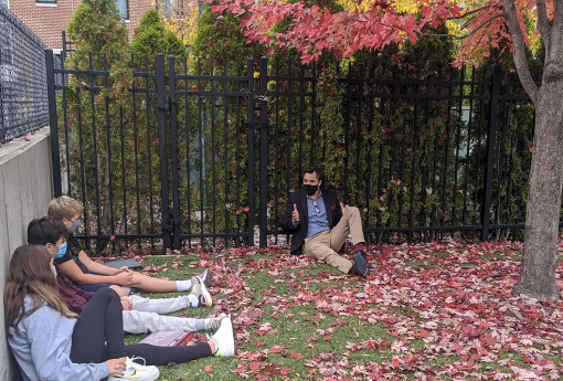 Man sits under a tree talking with students 