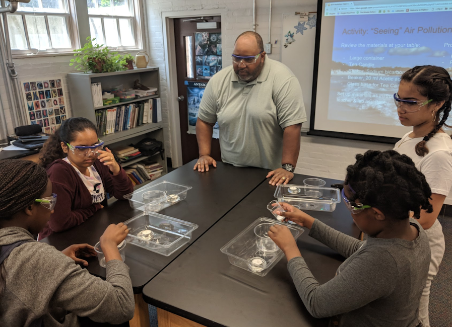 Older male teacher works with middle school students in a science lab.
