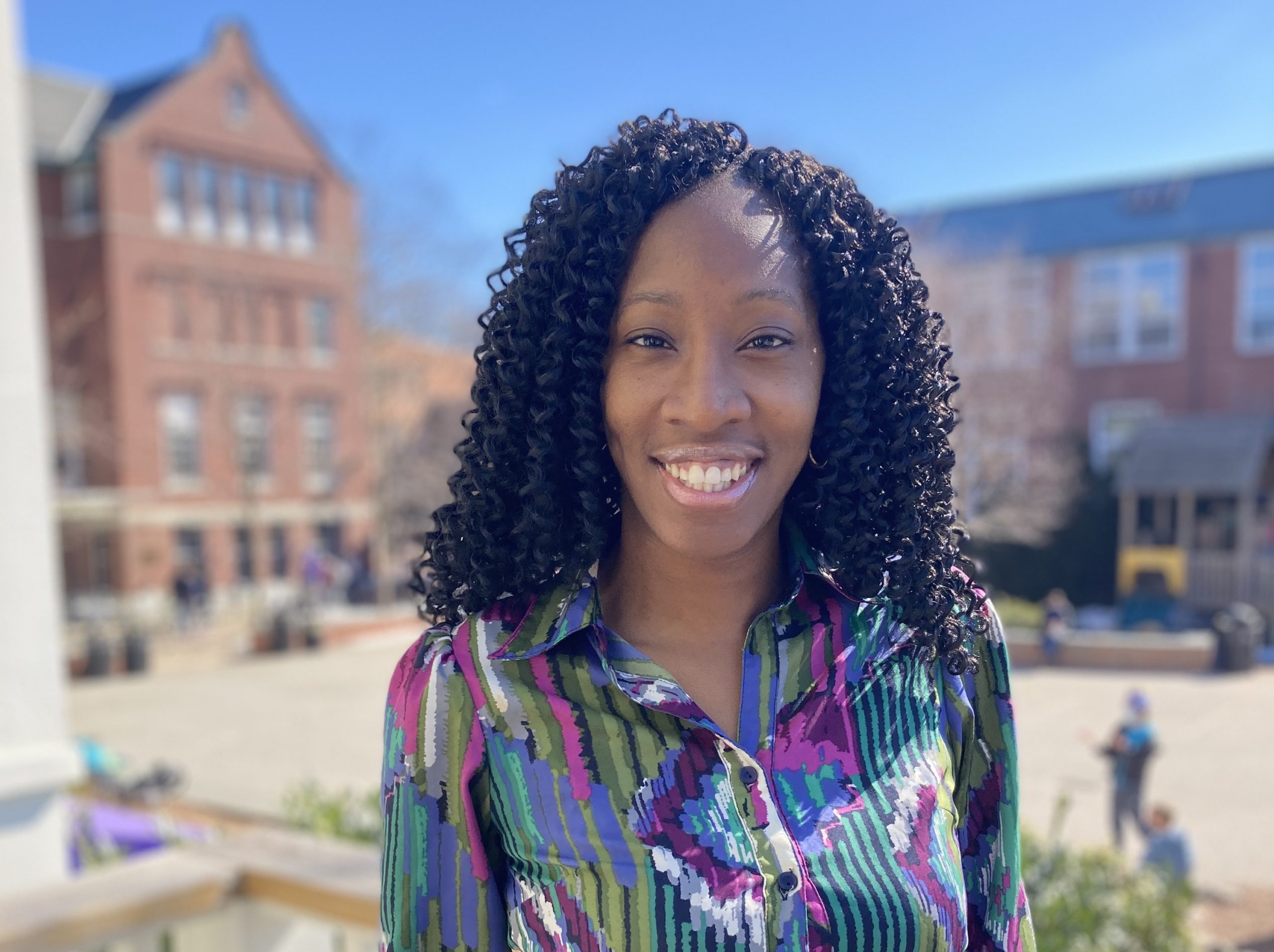 Young black adult smiles at camera as she stands in the school courtyard.