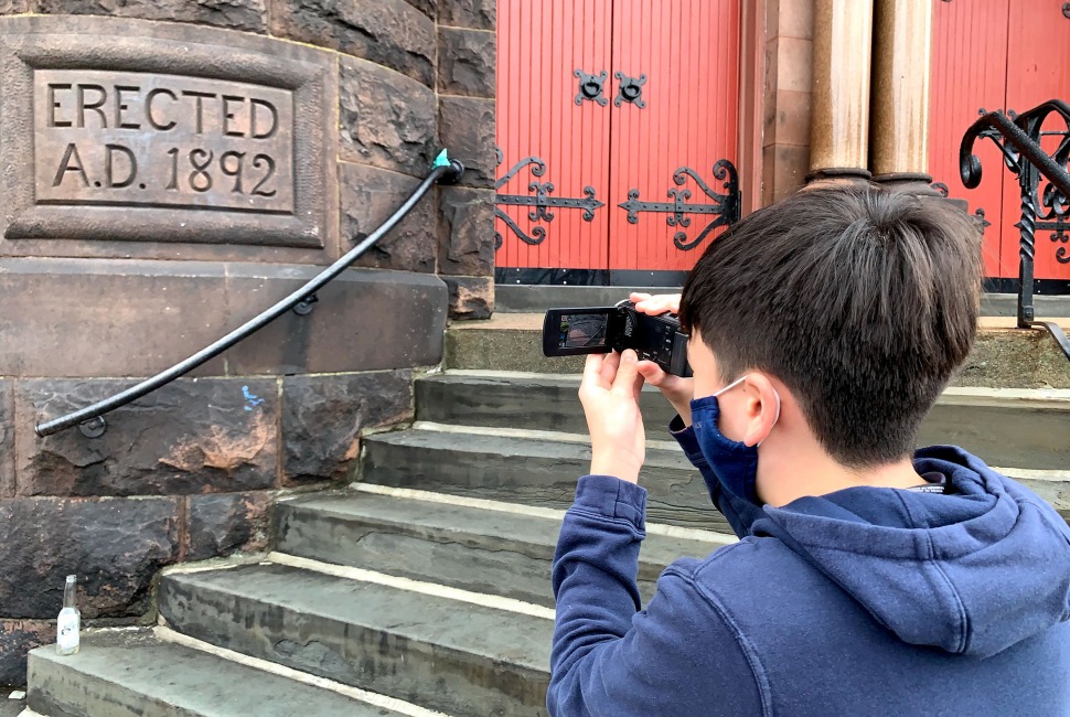 8th grade boy uses video camera to record historic building plaque.