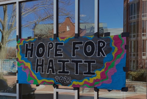 Colorful banner saying Hope for Haiti hung on windows of building. In the reflection of the window several other school buildings are shown.