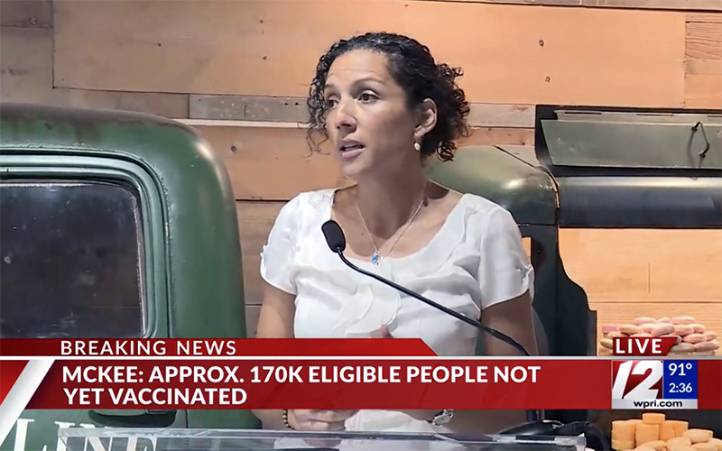 A still image from news coverage of Wheeler Nurse Judy Diaz speaking at the weekly COVID-19 briefing. Diaz is looking off camera and standing behind a clear podium.