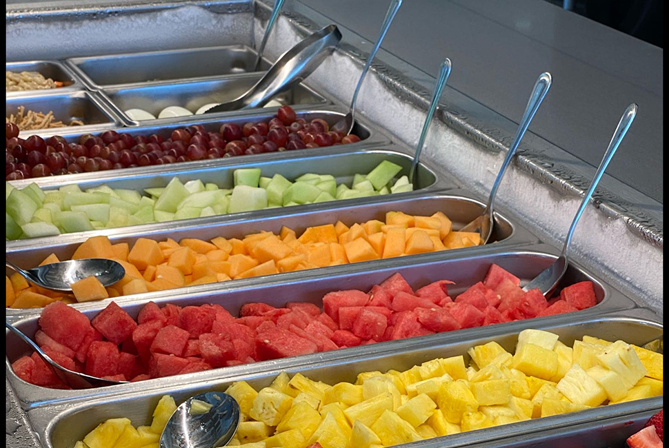 Image of a salad bar with fruit in metal containers.