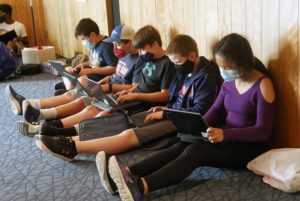 Students sitting on the ground all looking at and using laptop computers.