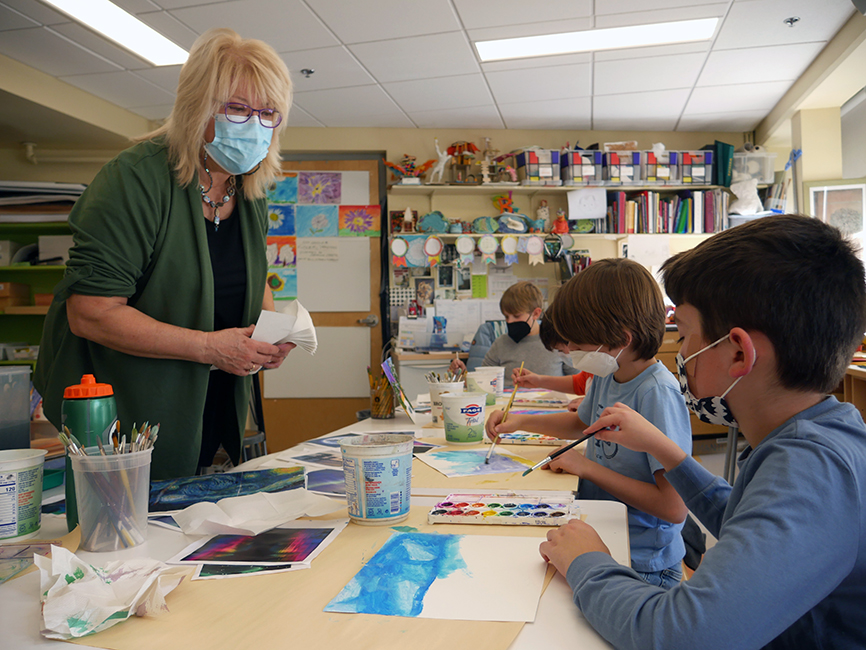 Teacher Bobbie Berking-Dalzell talks with a student who is painting their holiday card. Two other students paint in the background.