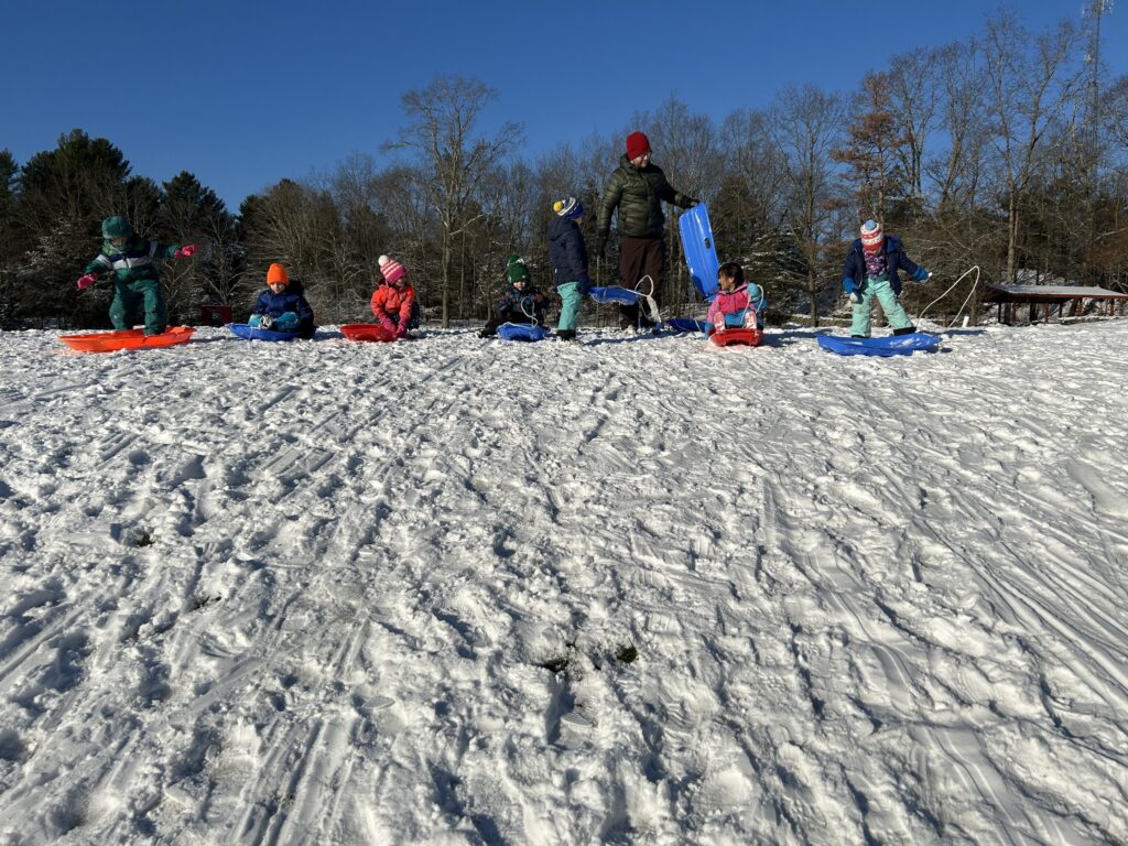Nest students at the top of the hill getting ready to slide down with their sleds.